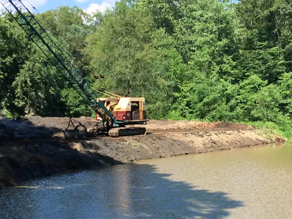 Dragline crane dredging a pond along a wooded shoreline
