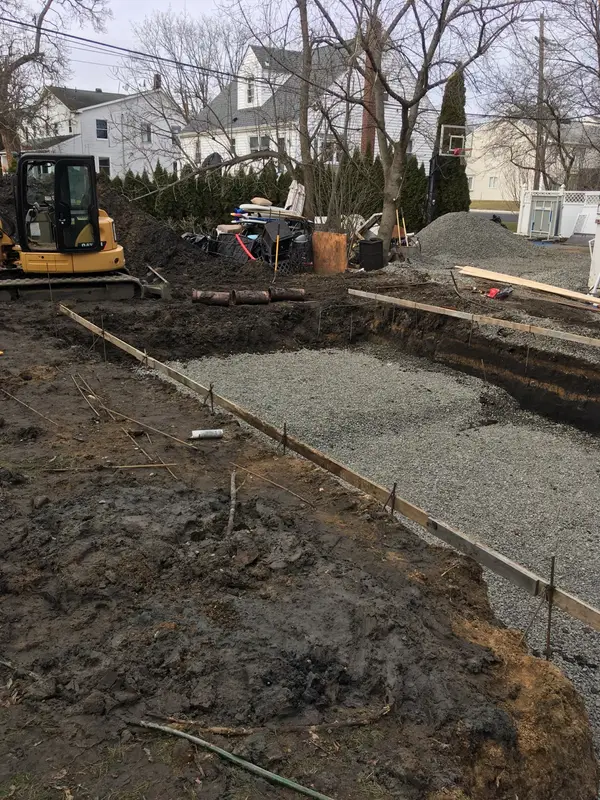 Septic drain field bed filled with stone next to a mini excavator in a residential backyard