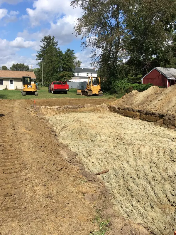 Excavated septic bed with a bulldozer and mini excavator parked on the lawn behind it