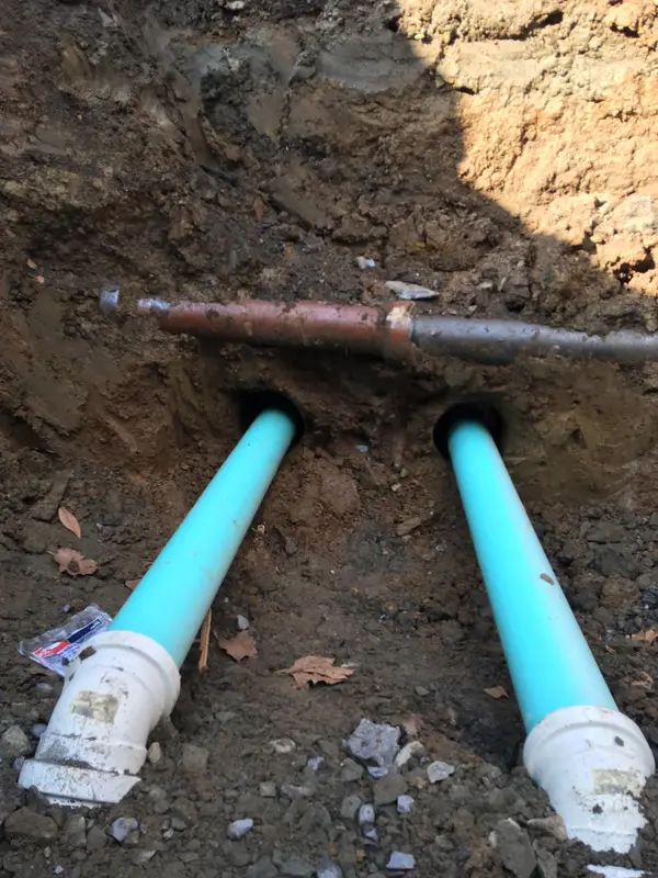 Two new PVC pipes installed in a trench beneath an existing utility line